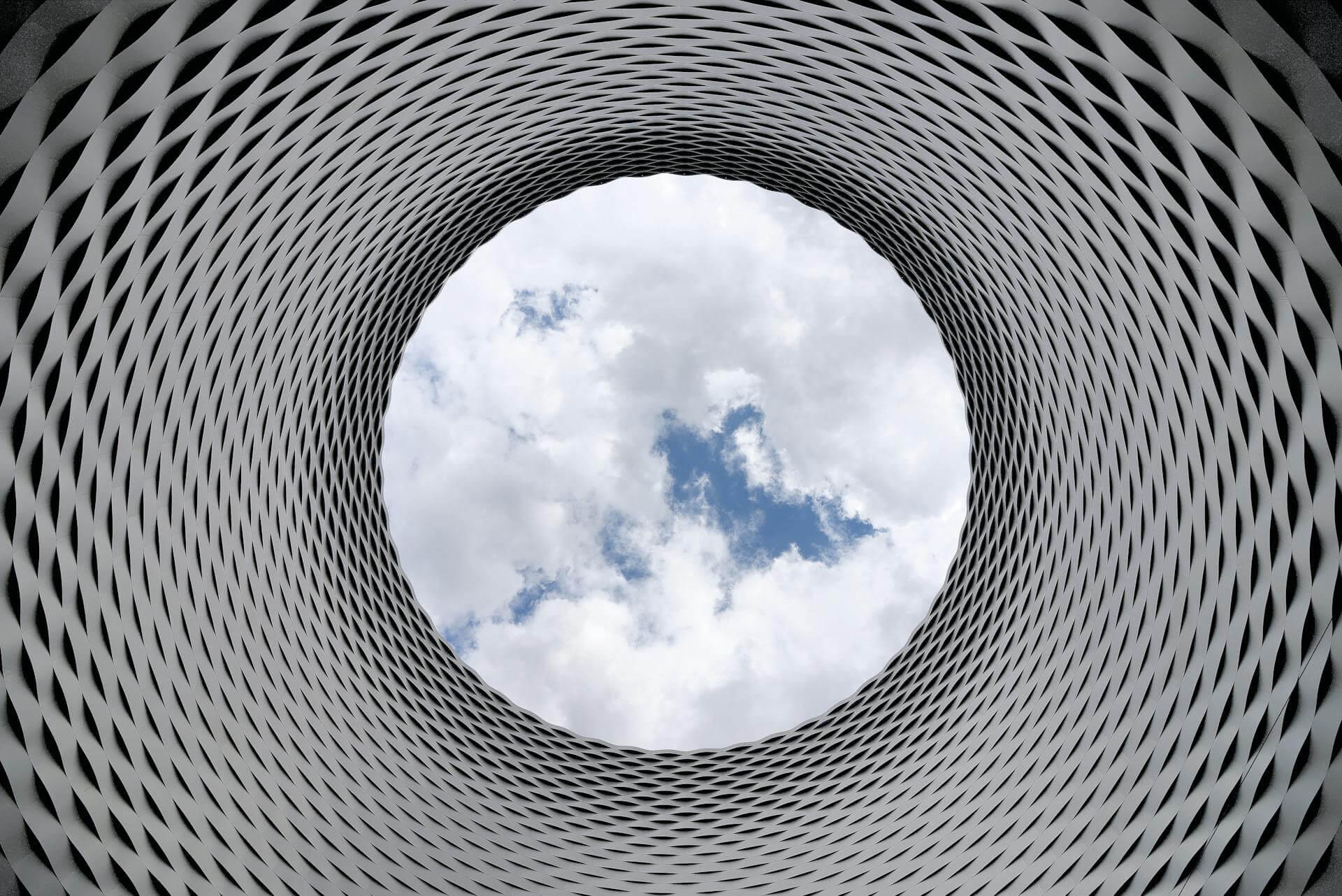 Low angle photography of grey and black tunnel overlooking white cloudy and blue sky.