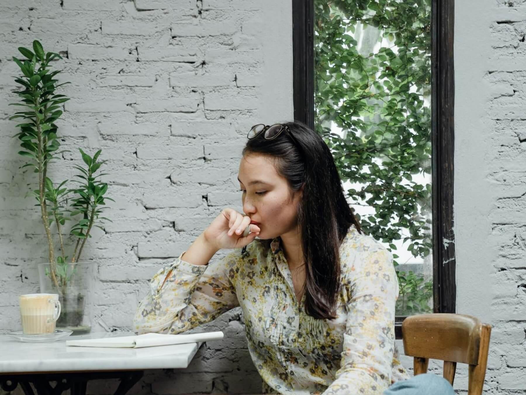 Focused young Asian woman thinking about project in cafeteria.