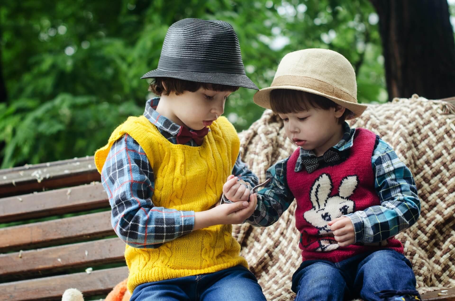Two Boys Sitting on Bench Wearing Hats and Long-sleeved Shirts